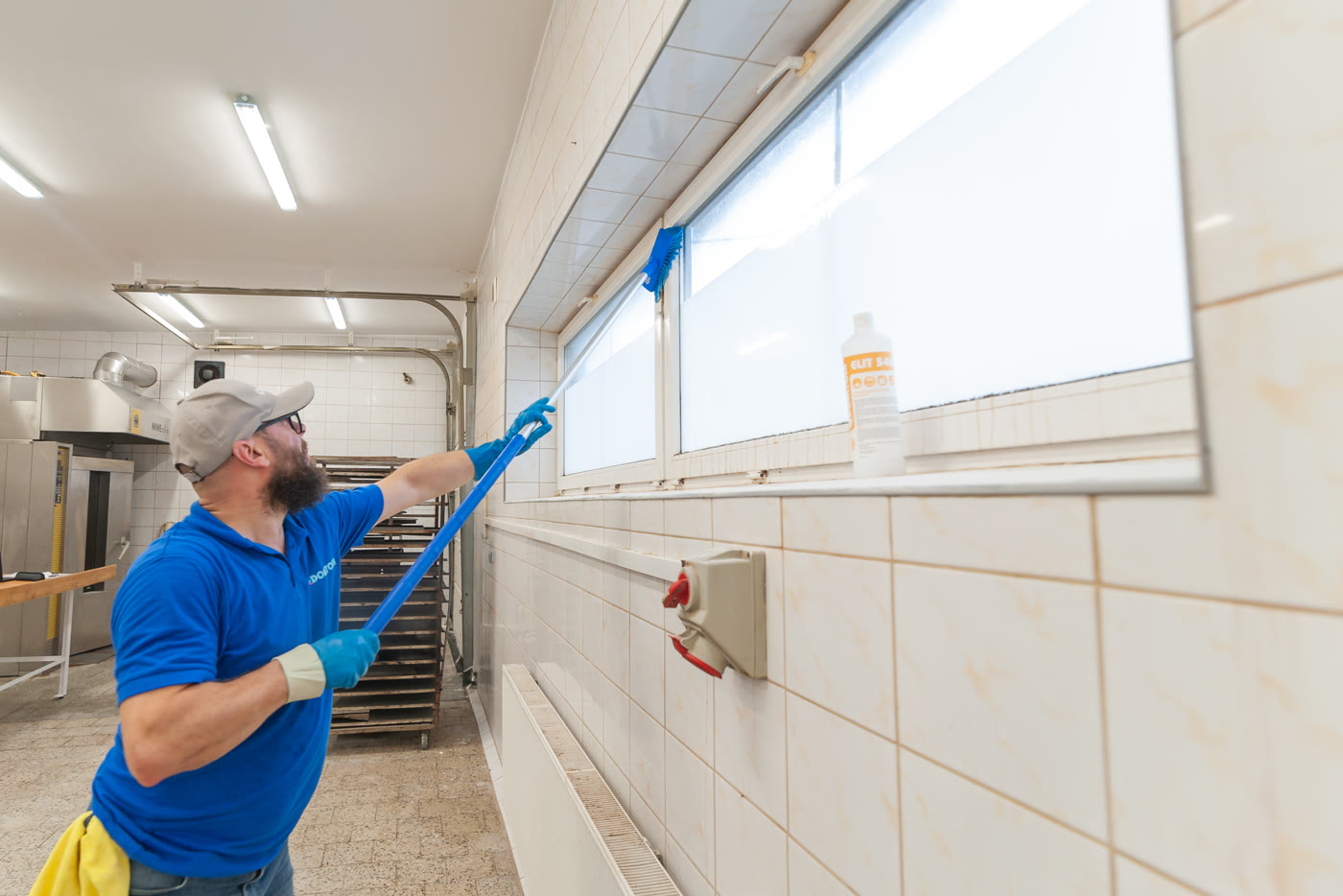 Doradca ELIT myje okna i ściany w hali produkcyjnej szczotką na wysięgniku